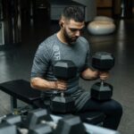 Adult man lifting dumbbells in a gym, focused on strength training workout.